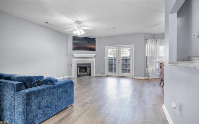 living room featuring a tile fireplace, ceiling fan, french doors, a textured ceiling, and light wood-type flooring