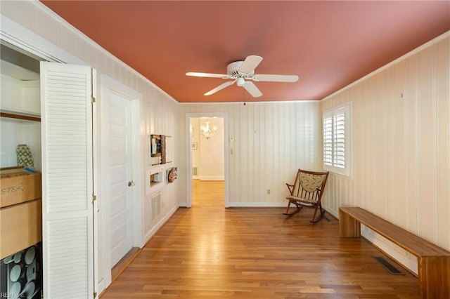 unfurnished room featuring light hardwood / wood-style flooring, ceiling fan with notable chandelier, and ornamental molding