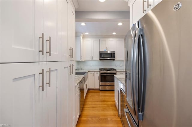 kitchen with light stone countertops, appliances with stainless steel finishes, decorative backsplash, light hardwood / wood-style floors, and white cabinetry