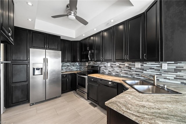 kitchen featuring a raised ceiling, sink, ceiling fan, stainless steel appliances, and light stone countertops