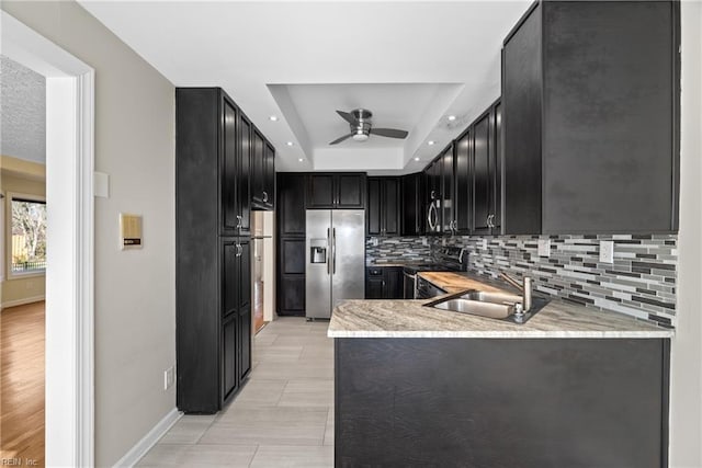 kitchen featuring a raised ceiling, light stone countertops, appliances with stainless steel finishes, and ceiling fan