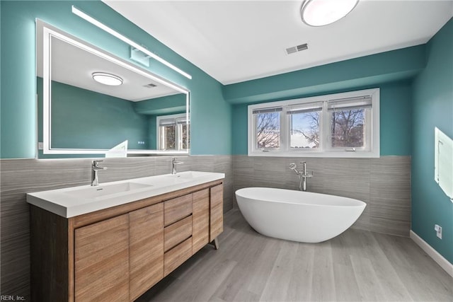 bathroom with hardwood / wood-style flooring, vanity, tile walls, and a tub to relax in