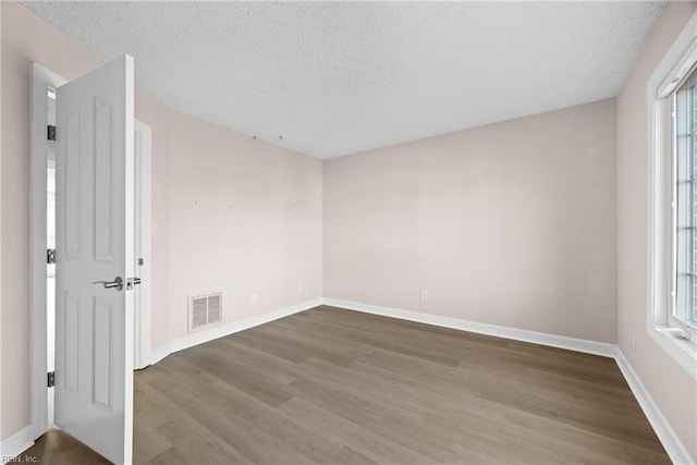 empty room with a wealth of natural light, wood-type flooring, and a textured ceiling