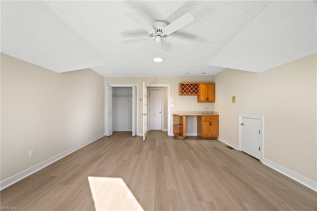 unfurnished living room featuring ceiling fan, bar area, a textured ceiling, and light hardwood / wood-style floors