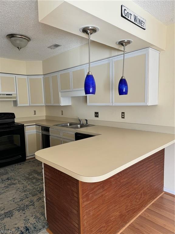 kitchen with kitchen peninsula, sink, decorative light fixtures, white cabinetry, and black / electric stove