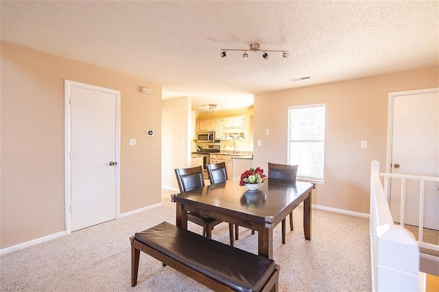 carpeted dining space featuring sink, a textured ceiling, and track lighting