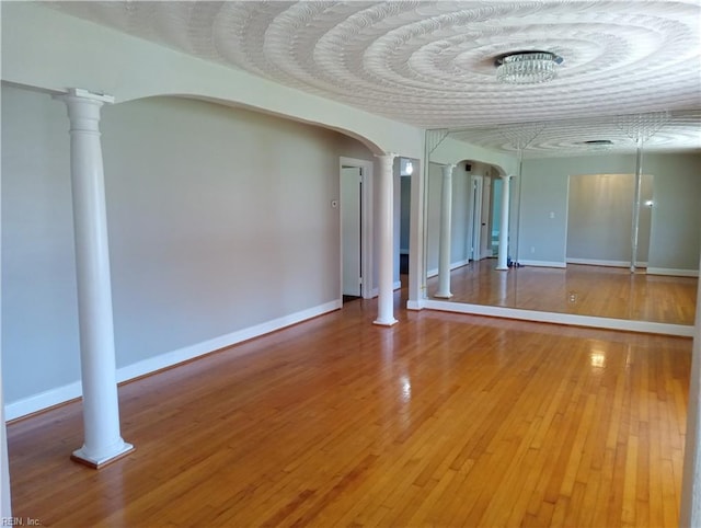 spare room featuring hardwood / wood-style floors and ornate columns