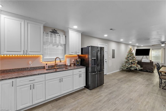 kitchen featuring dark stone counters, white cabinets, black fridge, sink, and ceiling fan