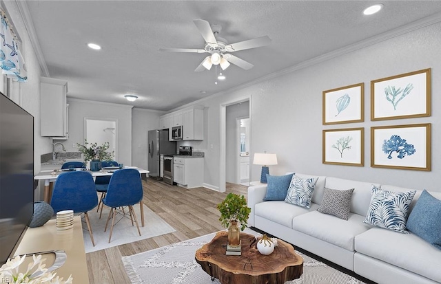 living room with a textured ceiling, light wood-type flooring, ceiling fan, and ornamental molding