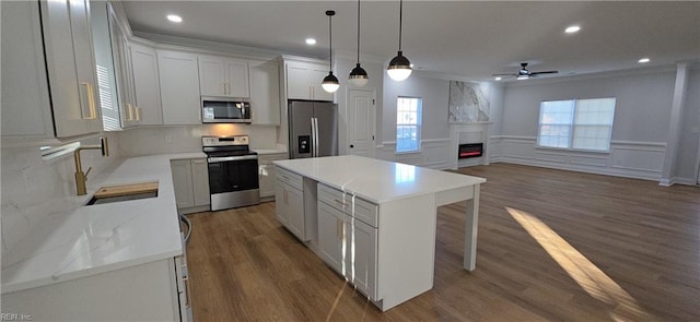 kitchen with white cabinetry, appliances with stainless steel finishes, hanging light fixtures, ornamental molding, and a center island