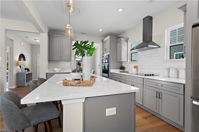 kitchen with gray cabinets, a kitchen island, stainless steel appliances, and wall chimney exhaust hood