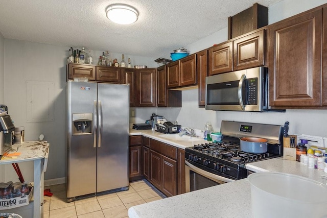 kitchen featuring dark brown cabinetry, sink, stainless steel appliances, a textured ceiling, and light tile patterned floors