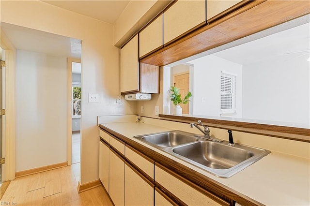 kitchen with baseboards, light countertops, cream cabinets, light wood-style floors, and a sink