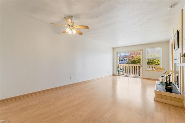 unfurnished living room with a ceiling fan, baseboards, light wood-style flooring, a fireplace with raised hearth, and a textured ceiling