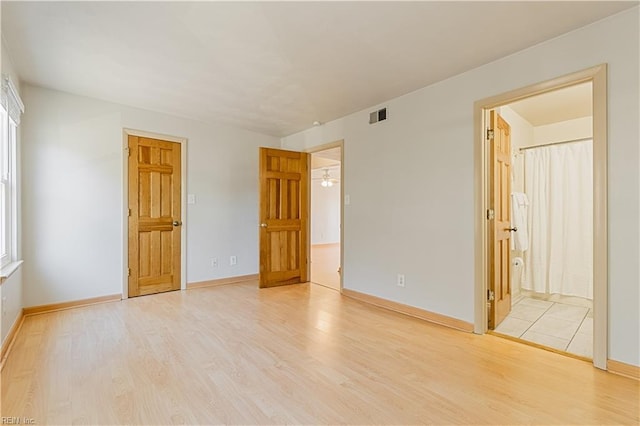 unfurnished bedroom with visible vents, connected bathroom, light wood-type flooring, and baseboards