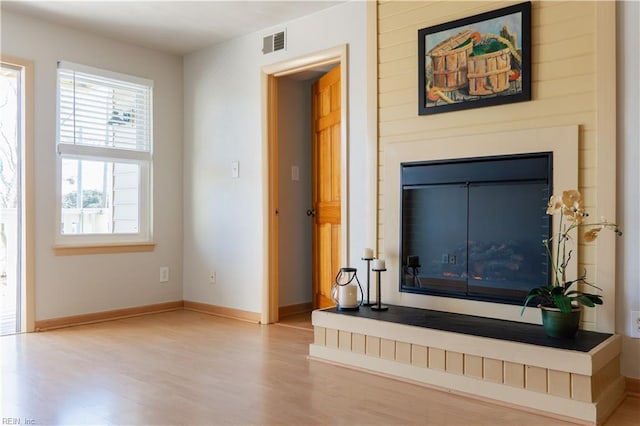 unfurnished living room featuring visible vents, a fireplace with raised hearth, baseboards, and wood finished floors