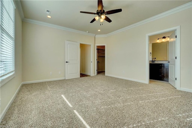 unfurnished bedroom with a walk in closet, ceiling fan, ornamental molding, connected bathroom, and light colored carpet