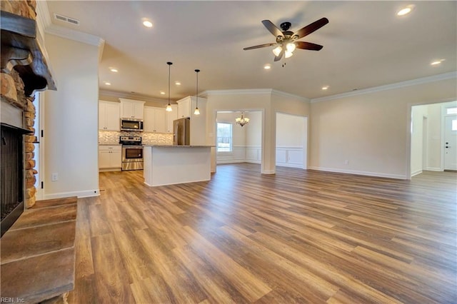 unfurnished living room featuring ceiling fan with notable chandelier, light hardwood / wood-style floors, a stone fireplace, and ornamental molding