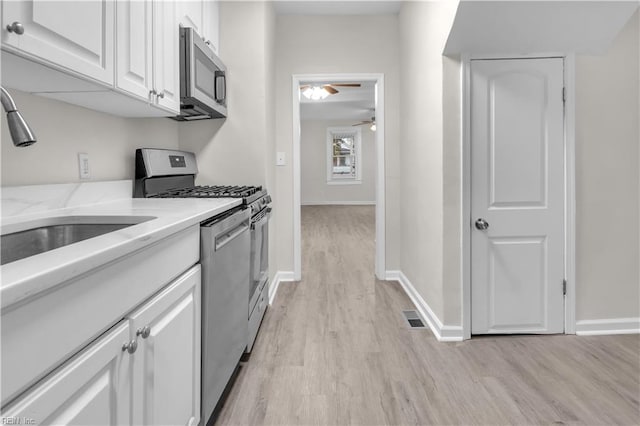 kitchen with white cabinetry, sink, ceiling fan, stainless steel appliances, and light wood-type flooring