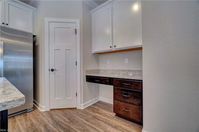 kitchen with light stone countertops, stainless steel fridge, white cabinets, built in desk, and light wood-type flooring