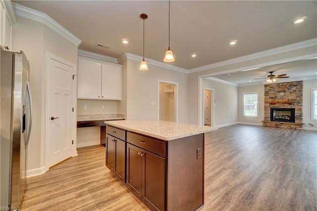 kitchen featuring light stone countertops, a stone fireplace, stainless steel fridge, crown molding, and white cabinets