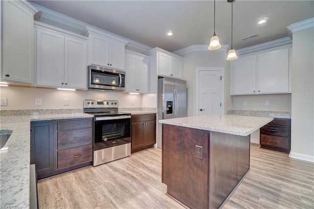 kitchen with appliances with stainless steel finishes, light stone counters, ornamental molding, decorative light fixtures, and white cabinets