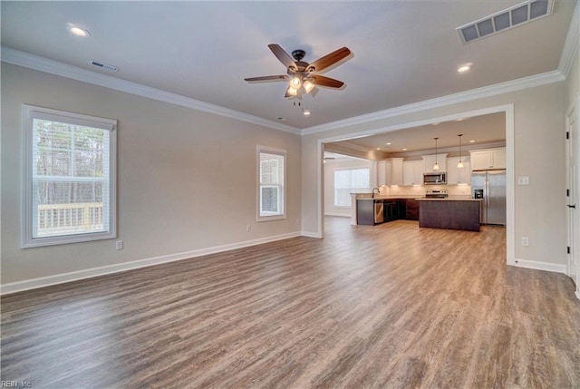 unfurnished living room featuring a healthy amount of sunlight, hardwood / wood-style flooring, ceiling fan, and crown molding