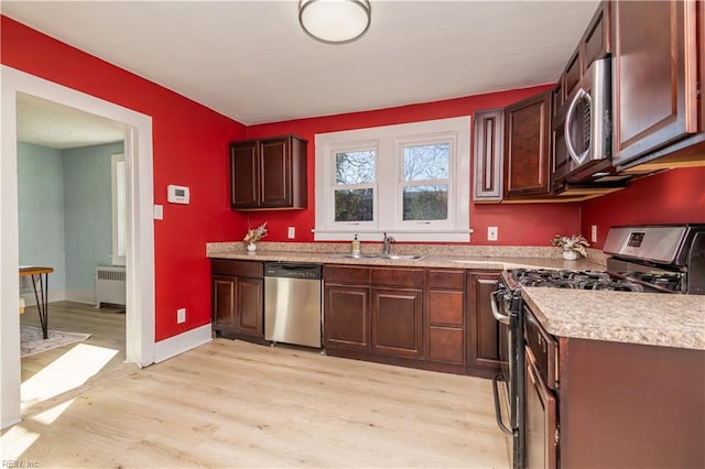 kitchen with radiator, sink, appliances with stainless steel finishes, and light hardwood / wood-style flooring