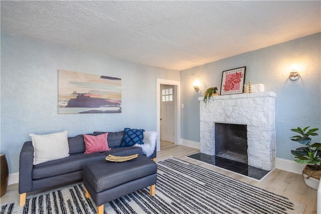 living room featuring a stone fireplace, light wood-type flooring, and a textured ceiling