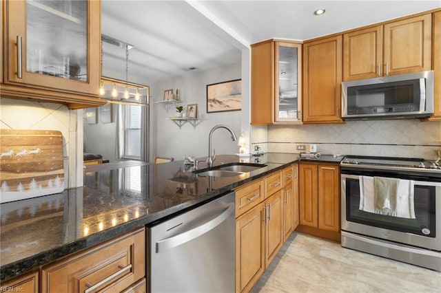 kitchen featuring backsplash, dark stone counters, sink, appliances with stainless steel finishes, and decorative light fixtures