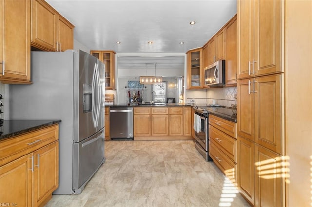 kitchen with backsplash, dark stone counters, appliances with stainless steel finishes, decorative light fixtures, and kitchen peninsula