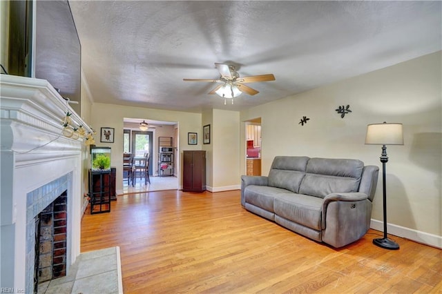 living room featuring ceiling fan, light hardwood / wood-style floors, and a brick fireplace