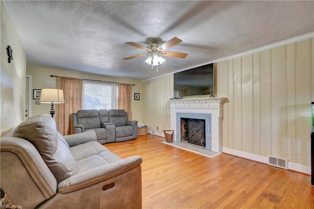 living room with a textured ceiling, ceiling fan, crown molding, light hardwood / wood-style flooring, and a fireplace