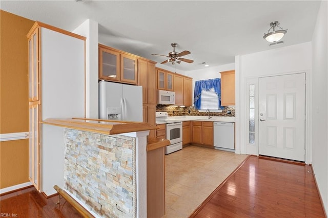 kitchen with decorative backsplash, kitchen peninsula, white appliances, ceiling fan, and light hardwood / wood-style flooring