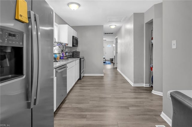 kitchen with light stone countertops, white cabinets, stainless steel appliances, and light hardwood / wood-style floors