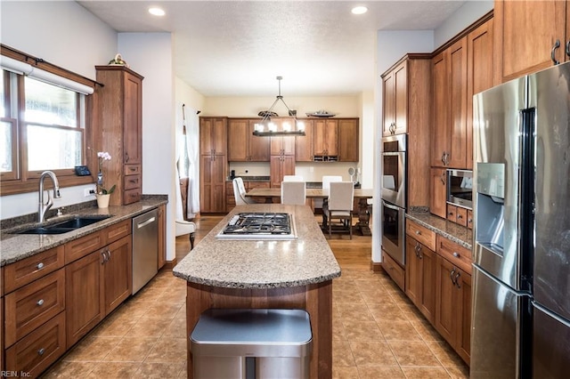 kitchen with a center island, sink, hanging light fixtures, appliances with stainless steel finishes, and light stone counters