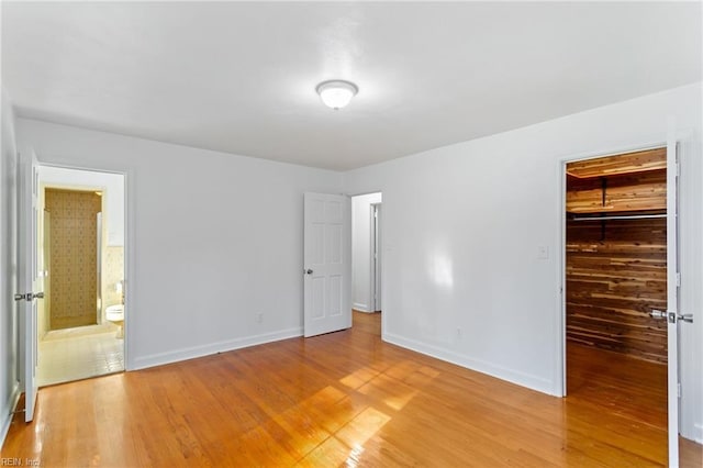 unfurnished bedroom with wooden walls, hardwood / wood-style flooring, a spacious closet, connected bathroom, and a closet