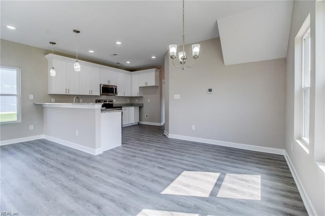 kitchen with hanging light fixtures, kitchen peninsula, appliances with stainless steel finishes, white cabinets, and hardwood / wood-style flooring