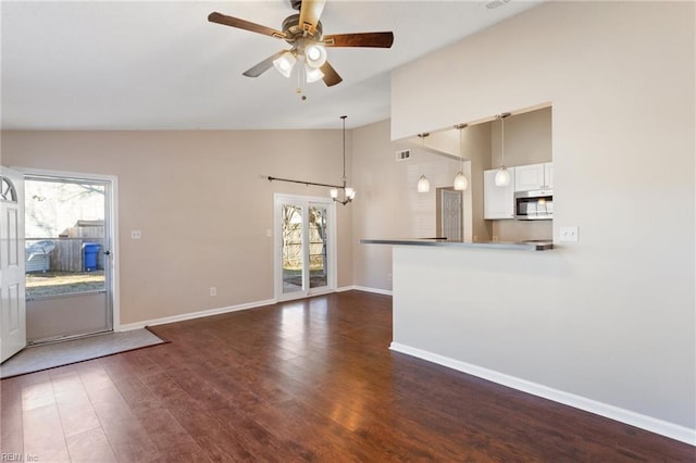 unfurnished living room featuring ceiling fan with notable chandelier, lofted ceiling, and dark wood-type flooring