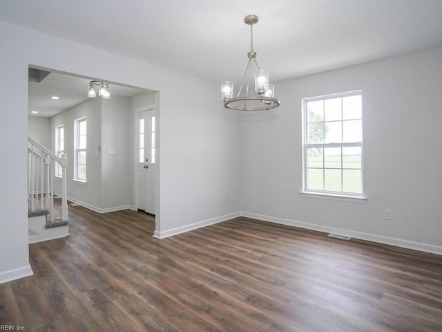 empty room featuring a wealth of natural light, dark hardwood / wood-style flooring, and an inviting chandelier