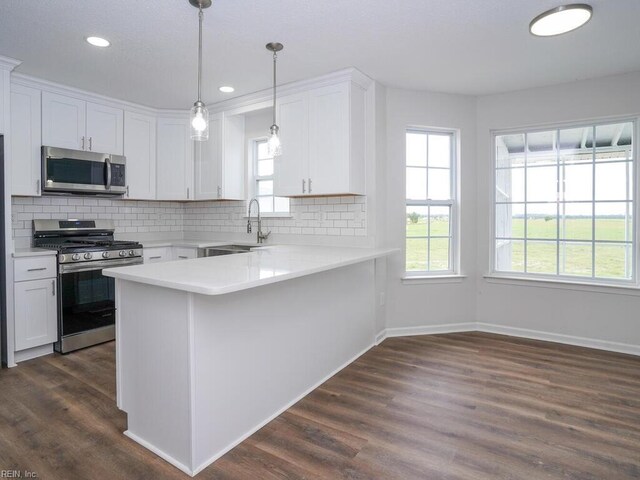 kitchen featuring kitchen peninsula, white cabinets, decorative light fixtures, and appliances with stainless steel finishes