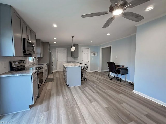 kitchen with sink, stainless steel appliances, light stone counters, decorative light fixtures, and a kitchen island