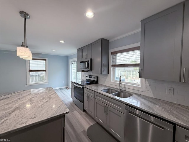 kitchen with appliances with stainless steel finishes, ornamental molding, sink, pendant lighting, and light hardwood / wood-style flooring