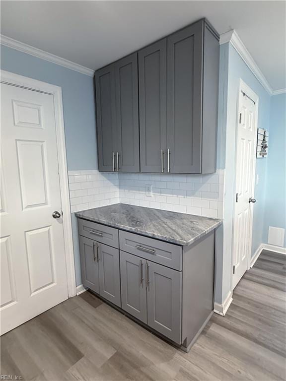 kitchen with gray cabinetry, dark stone countertops, crown molding, and light hardwood / wood-style flooring