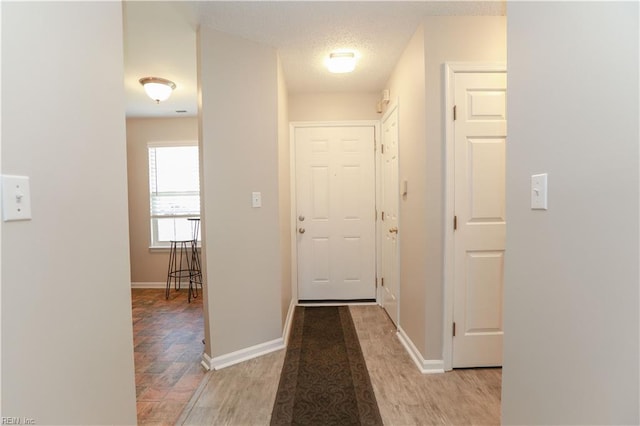 hallway with a textured ceiling and light hardwood / wood-style flooring