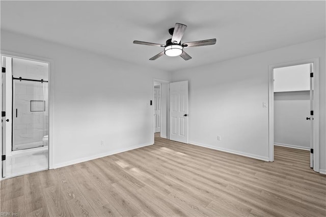 unfurnished bedroom with a walk in closet, ceiling fan, connected bathroom, light hardwood / wood-style floors, and a closet