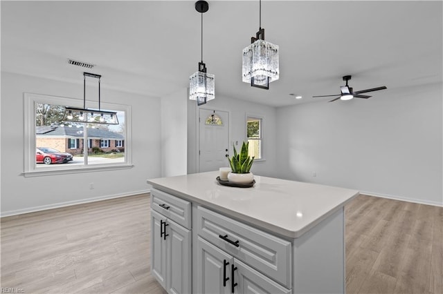 kitchen with light wood-type flooring, ceiling fan, white cabinets, a center island, and hanging light fixtures