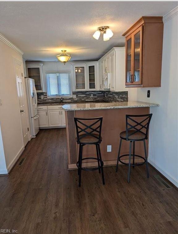 kitchen with white appliances, white cabinets, light stone countertops, a kitchen bar, and kitchen peninsula