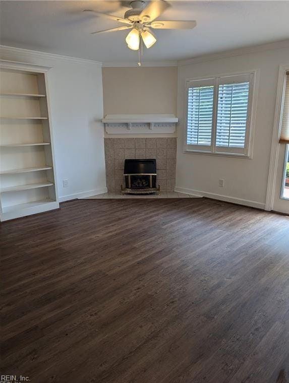 unfurnished living room with dark wood-type flooring, crown molding, built in shelves, ceiling fan, and a fireplace