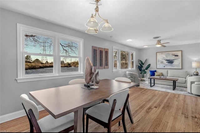 dining space with ceiling fan with notable chandelier and light hardwood / wood-style floors